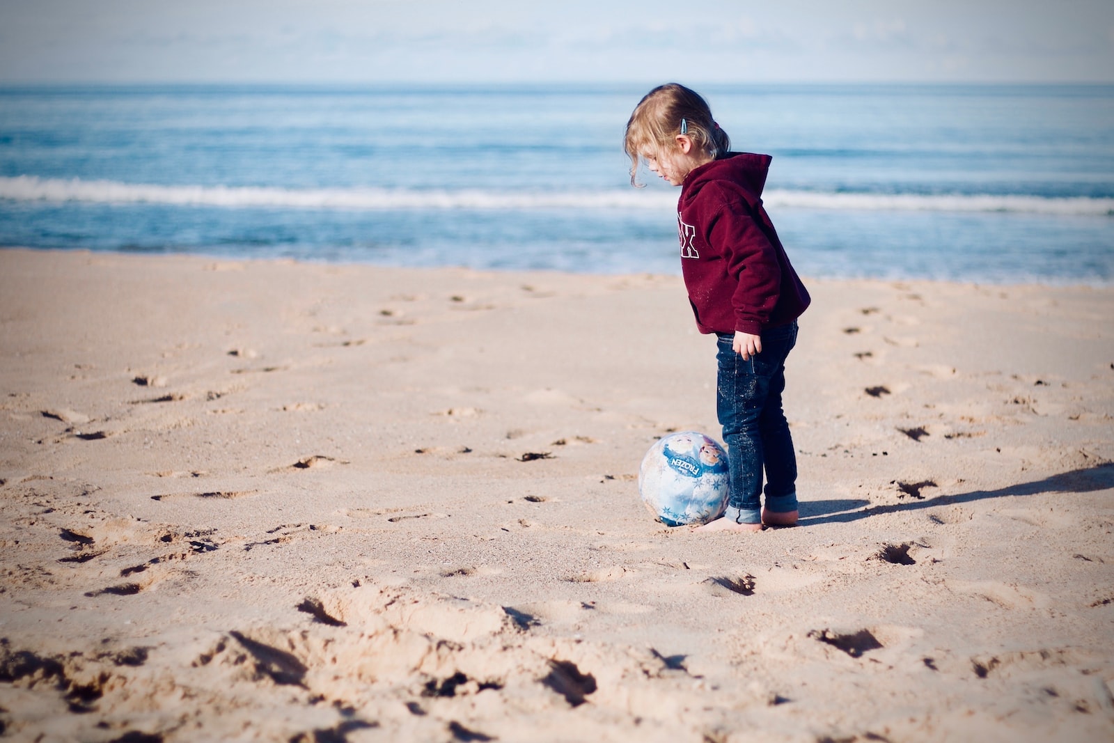girl standing beside ball on seashore